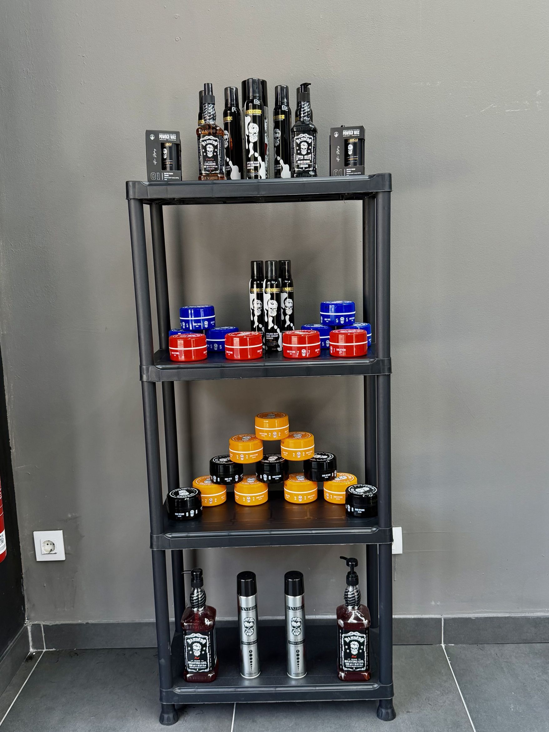 Estantería negra de cuatro baldas con botes de pomada azules, rojos y naranjas y botellas de producto de peinado.